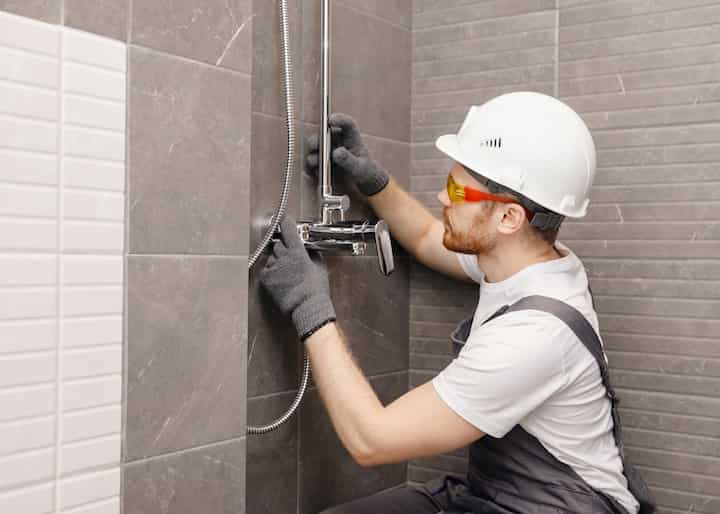 A bathroom remodeling contractor wearing a helmet installs fixtures in a shower.